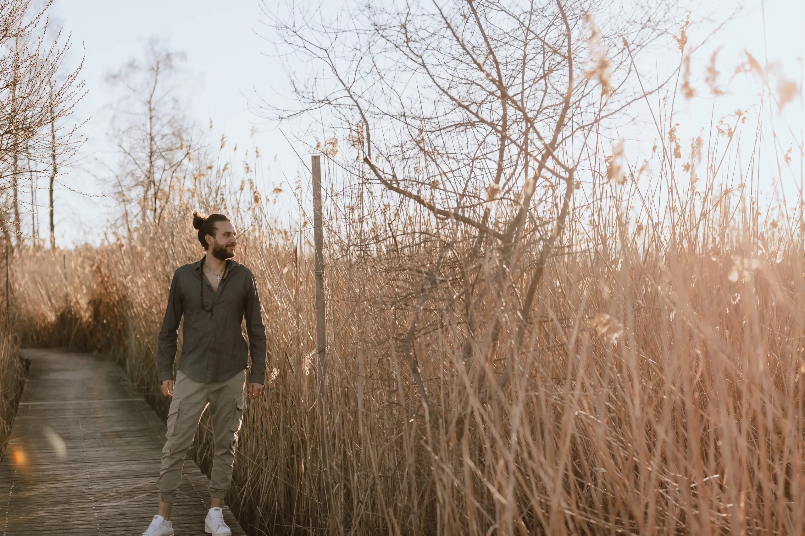 Fabio Sinicropi, initiateur du Vivant, debout avec sérénité sur un ponton en bois au cœur d'une nature sauvage entourée de hauts roseaux, illustrant le retour à soi.